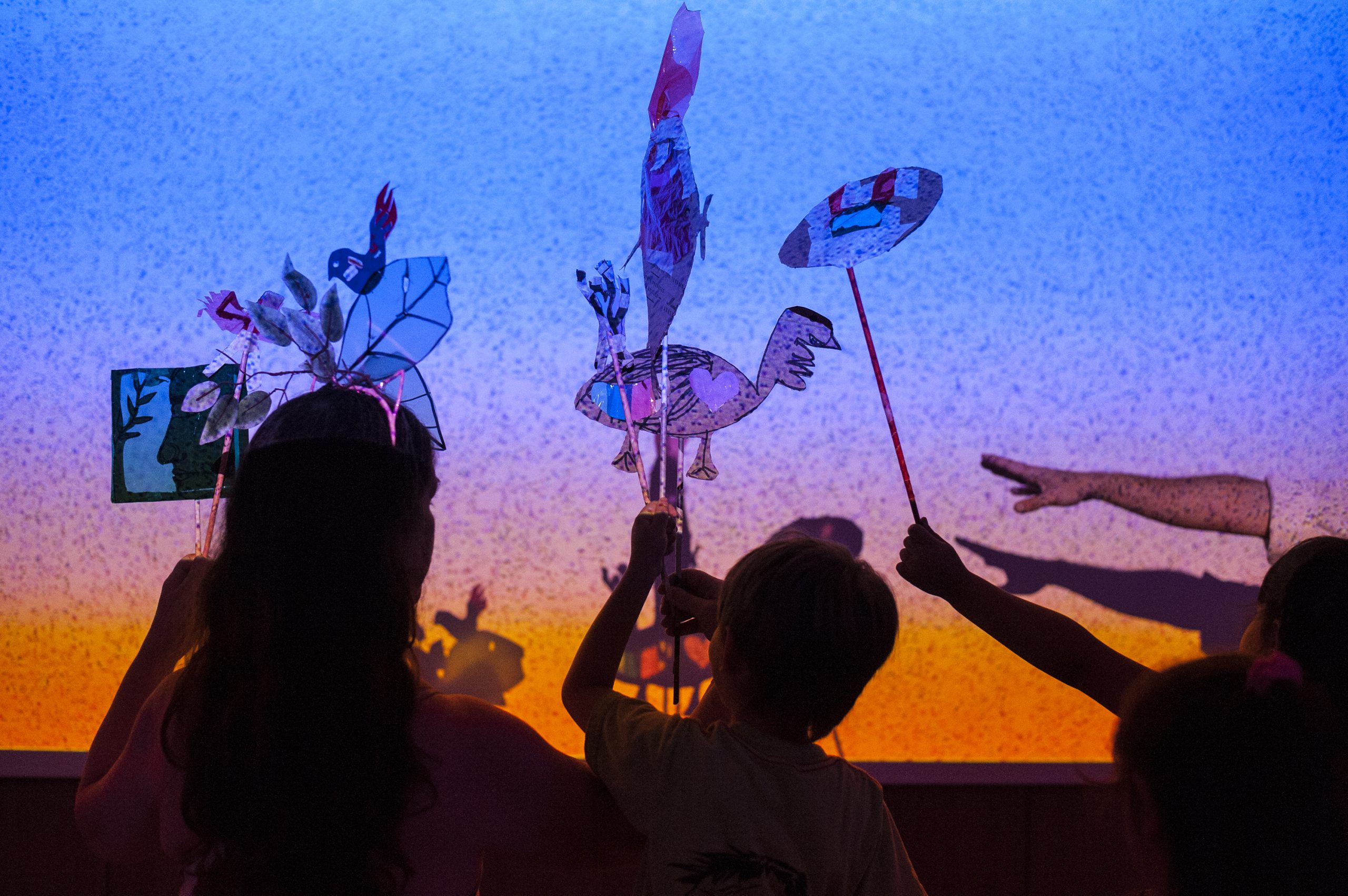 Foto muestra un momento durante el show donde hay niños y familias proyectando sus creaciones en un fondo de colores tipo cielo estrellado