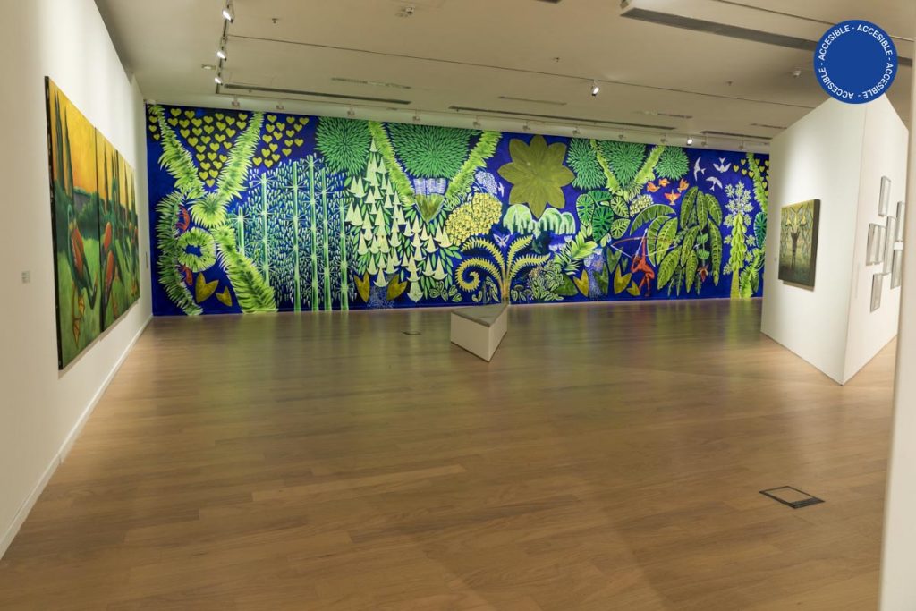 Foto de sala de la exposición Manifiesto verde. Sobre una de las paredes puede apreciarse un gran mural de Florencia Bohtlingk, pintado con imágenes de flora y vegetación.