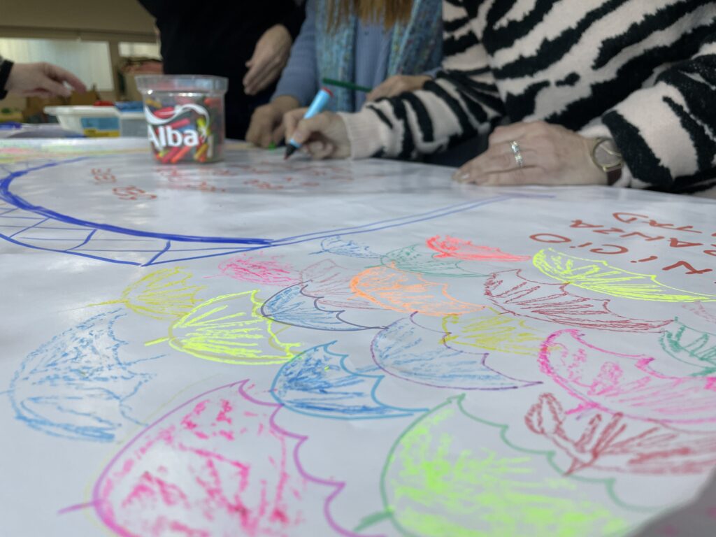 En la imagen se ven las manos de dos personas pintando con marcadores sobre una mesa.