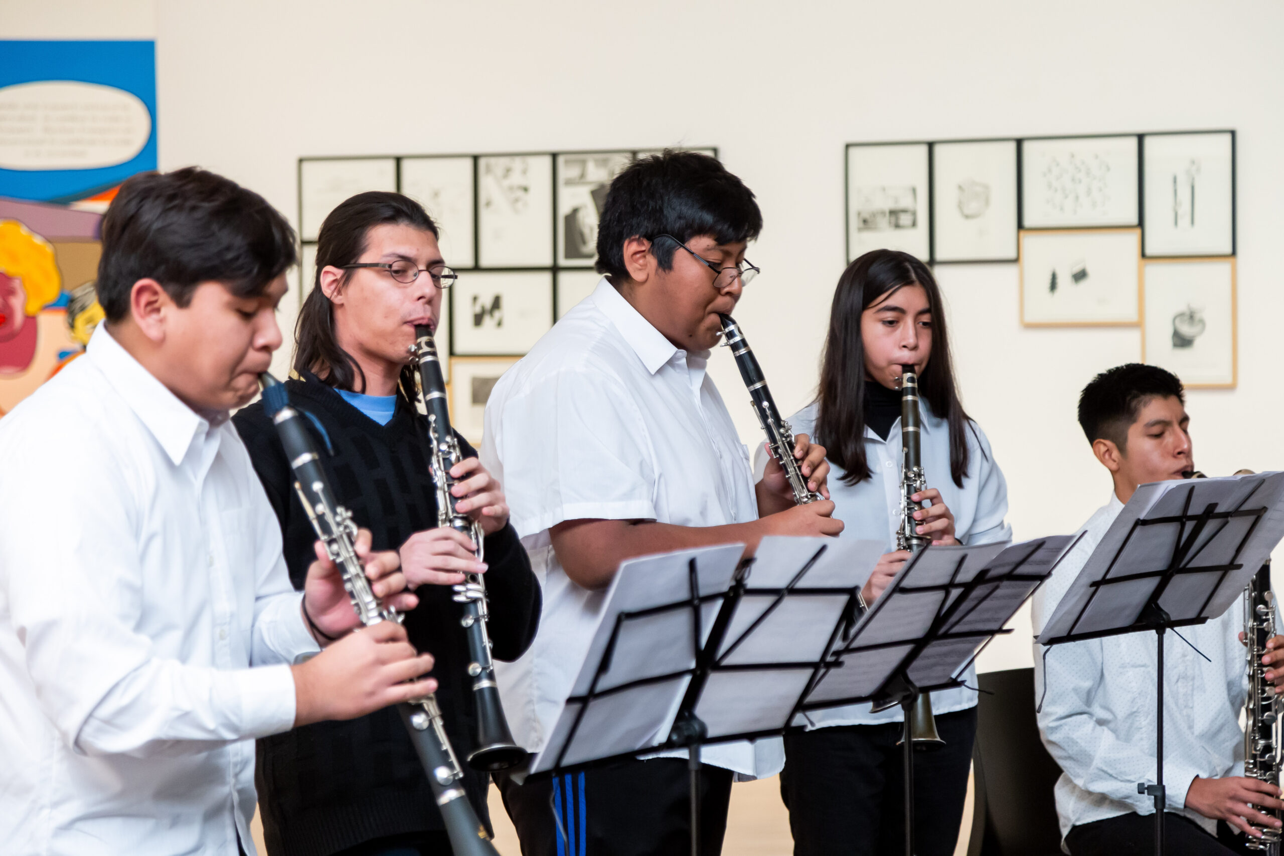 La imagen muestra un grupo de jóvenes tocando instrumentos en una sala de exposiciones del Museo.