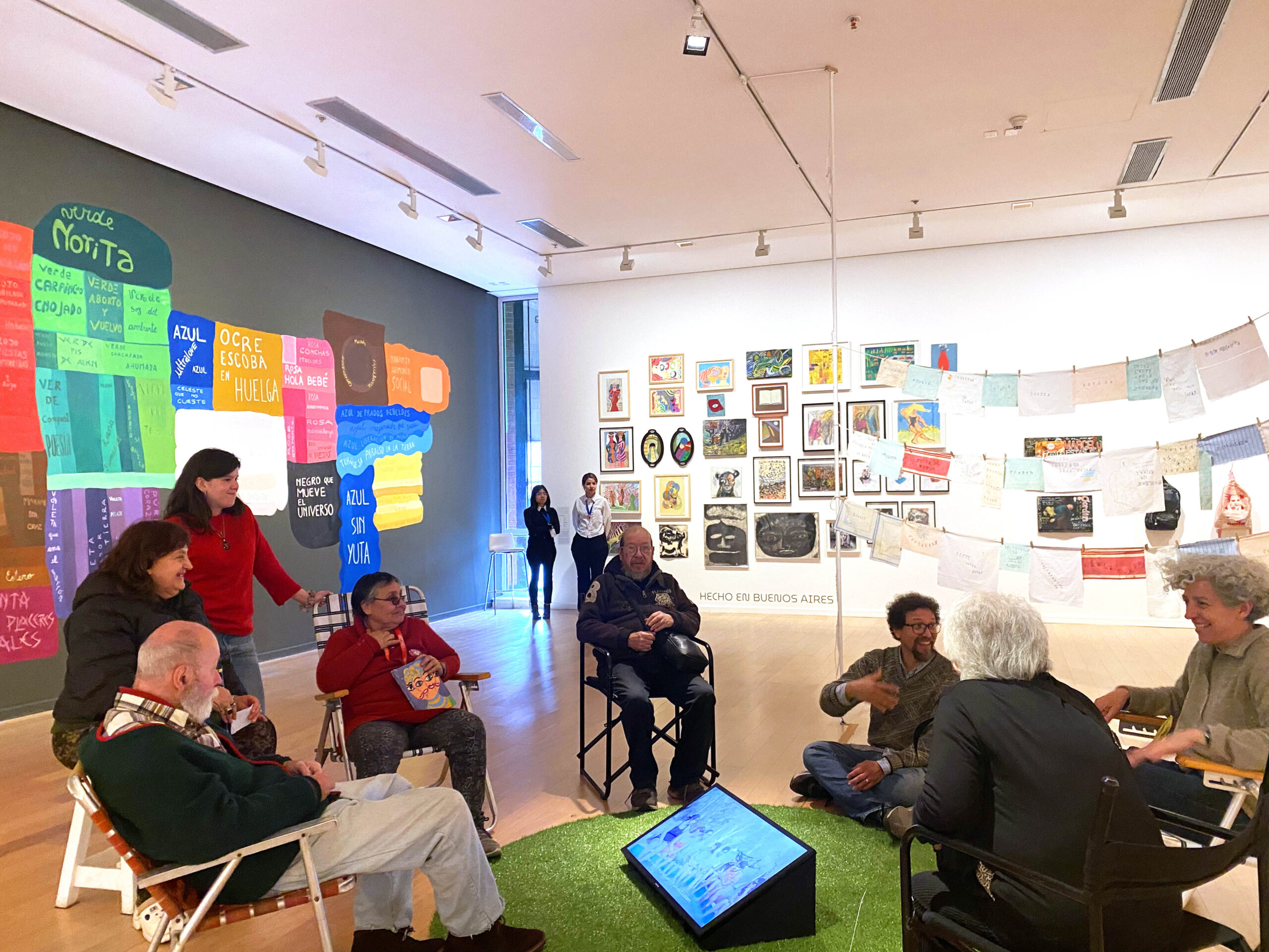 La imagen muestra a los participantes del Aula Cósmica del Bajo reunidos en ronda en la exposición El aprendizaje infinito.