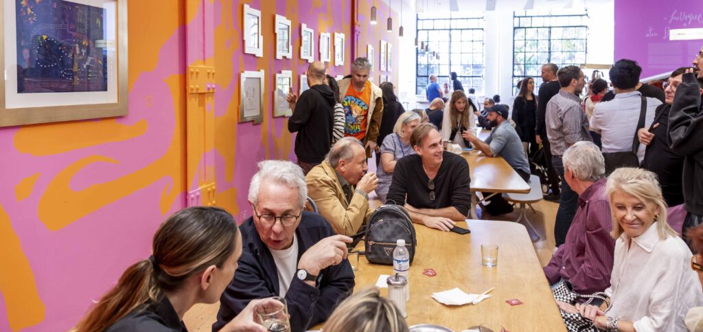 En la fotografía se observa un grupo de personas en el Café Moderno, tomando café, conversando y algunos mirando las obras de la intervención en el espacio y exposición Bárbara Bianca LaVogue: Tu presencia en mí que allí se encuentra expuesta.