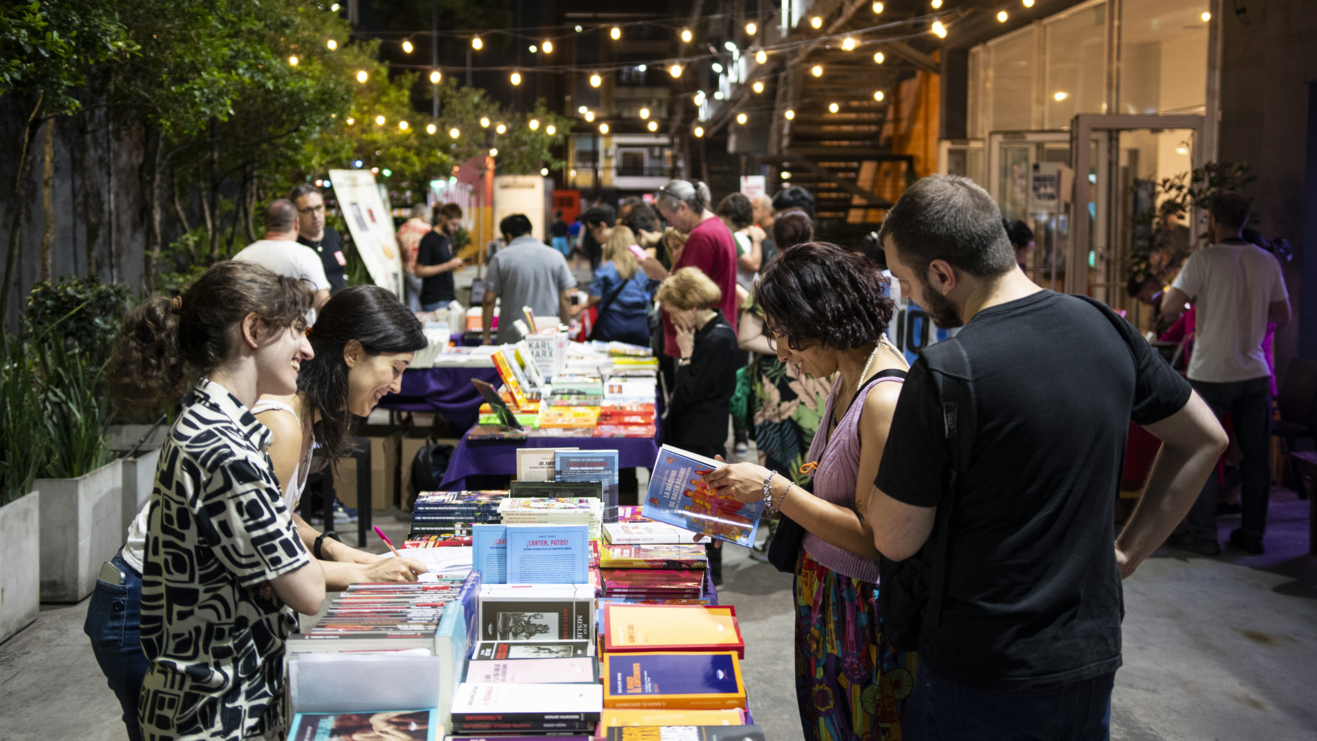 En la fotografía a color se observa un grupo de personas mirando y leyendo algunos de los libros en los diversos puestos de la Feria del Libro de Humanidades y Ciencias Sociales en el Museo Moderno