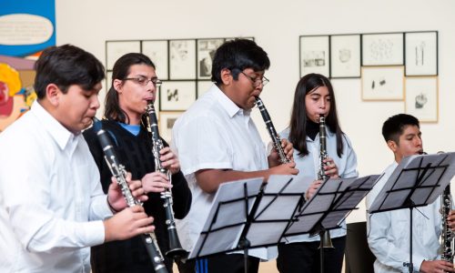 La imagen muestra un grupo de jóvenes tocando instrumentos en una sala de exposiciones del Museo.