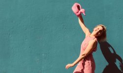 Mujer sonriente en overol rosa, jugando con una regadera sobre una bañera colorida