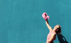 Una mujer sonriente, en overol rosa, juega con una regadera sobre una bañera colorida.